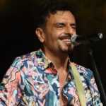 Davide de Marinis con microfono su sfondo nero con fumo giallo