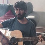 Nicolò Cavalchini con chitarra e divano sullo sfondo