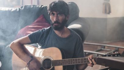 Nicolò Cavalchini con chitarra e divano sullo sfondo