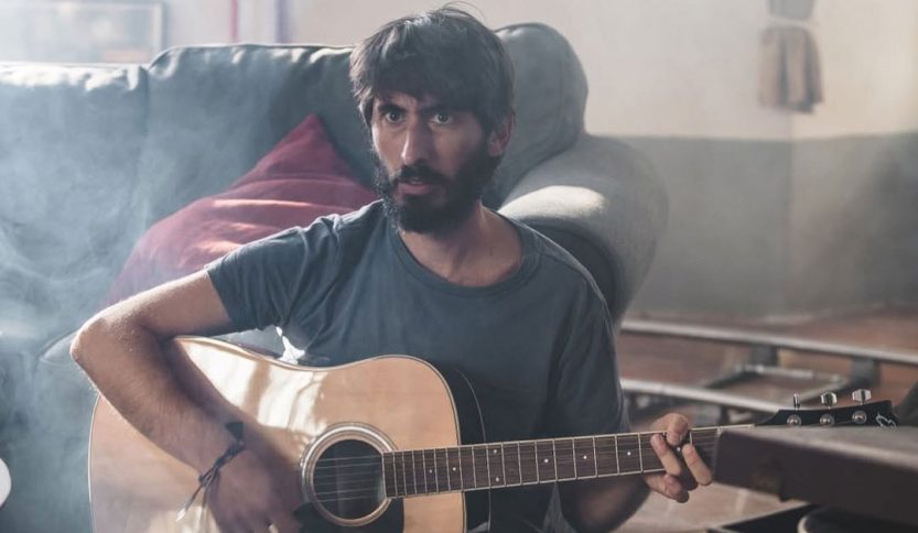 Nicolò Cavalchini con chitarra e divano sullo sfondo