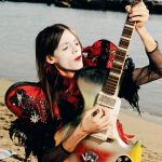 lucio corsi e la chitarra su una spiaggia