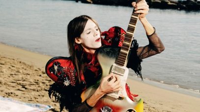 lucio corsi e la chitarra su una spiaggia