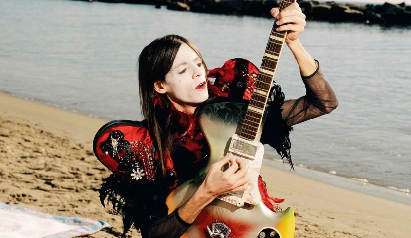 lucio corsi e la chitarra su una spiaggia