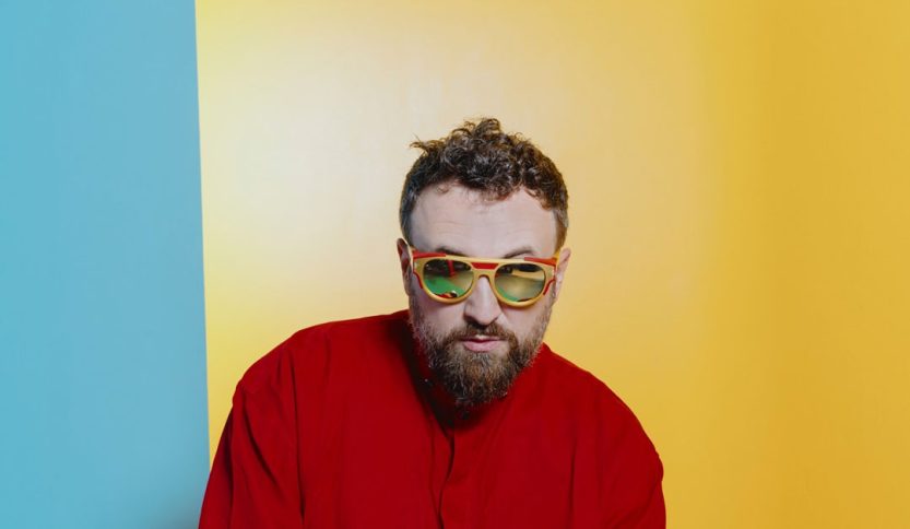 Dargen D'Amico in rosso con sfondo giallo e celeste